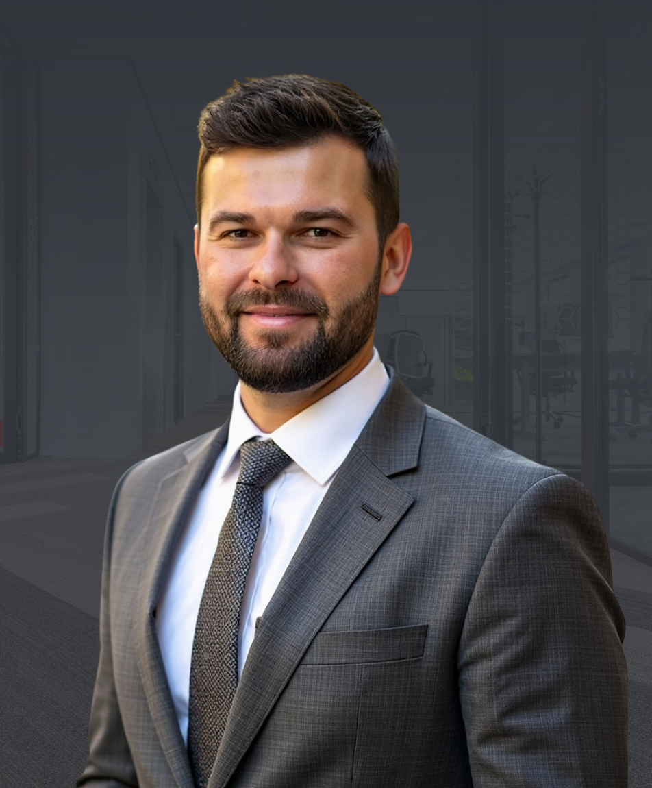 Professional portrait of a confident man in a gray suit and tie, standing in a modern office setting - used on the Contact page for Executive Edge Recruiting, where visitors are invited to connect about leadership opportunities.