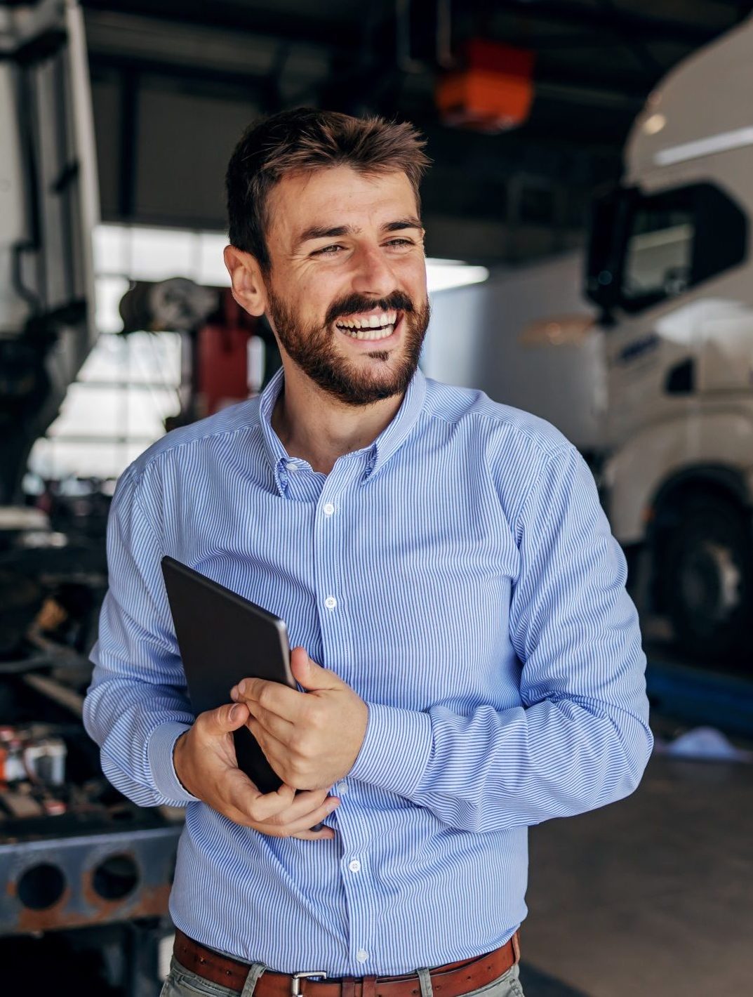 Smiling tradesman in a blue shirt holding a tablet in a workshop